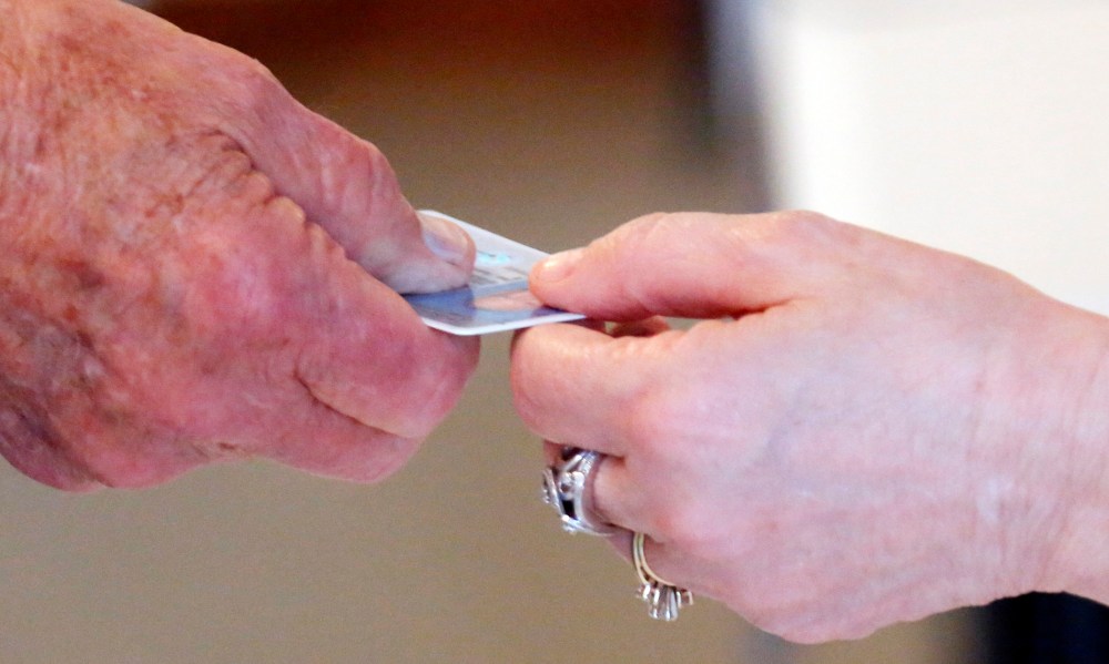 A Republican primary precinct worker hands back a voter's driver's license before handing over a voters access card in Madison, Miss., Tuesday, June 3, 2014.