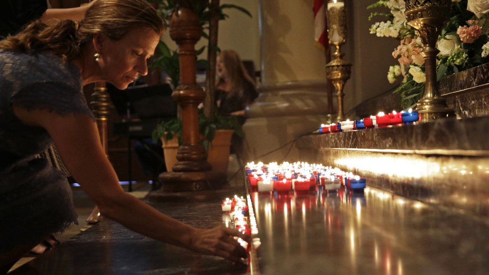A woman places a candle on the altar during a prayer service for the victims of The Grand 16 theater shooting at the Cathedral of St. John the Evangelist, in Lafayette, La., July 26, 2015. (Photo by Gerald Herbert/AP)