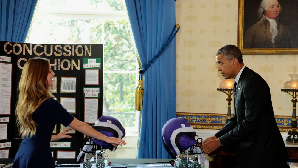 Maria Hanes, 19, of Santa Cruz, Calif., left, has President Barack Obama pull back a cushioned helmet as Obama toured the 2014 White House Science Fair exhibits that are on display in the State Dining Room of the White House in Washington, May 27, 2014.