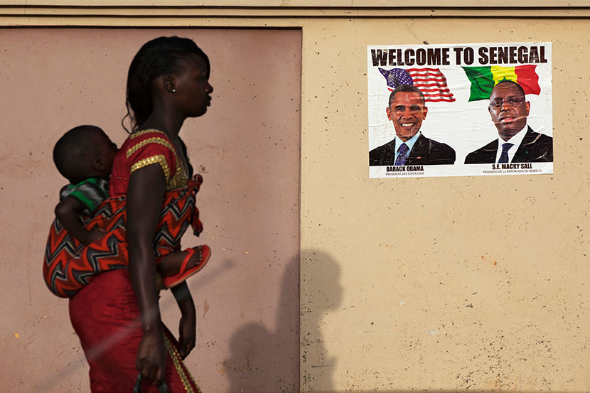 A woman carrying her baby on her back walks past a poster of U.S. President Barack Obama and Senegal's President Macky Sall before Obama's visit in Dakar June 26, 2013. (Photo by Joe Penney/Reuters)
