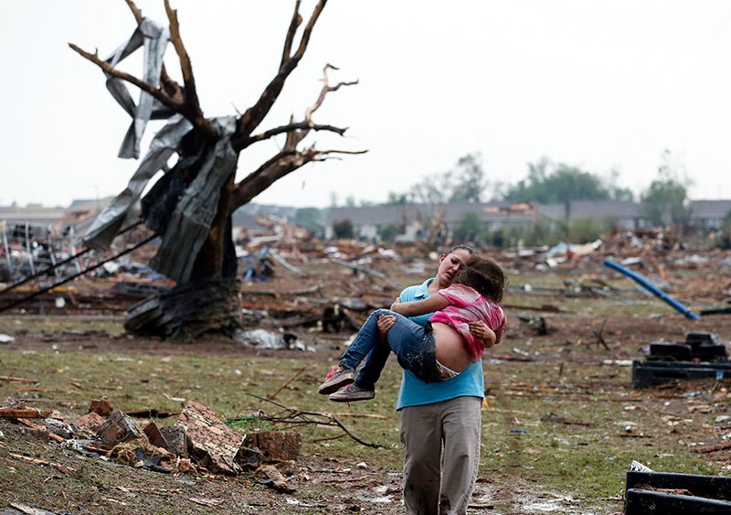 A woman carries a child through a field near the collapsed Plaza Towers Elementary School in Moore, Okla., Monday, May 20, 2013. A tornado as much as a mile wide with winds up to 200 mph roared through the Oklahoma City suburbs Monday, landing a direct...