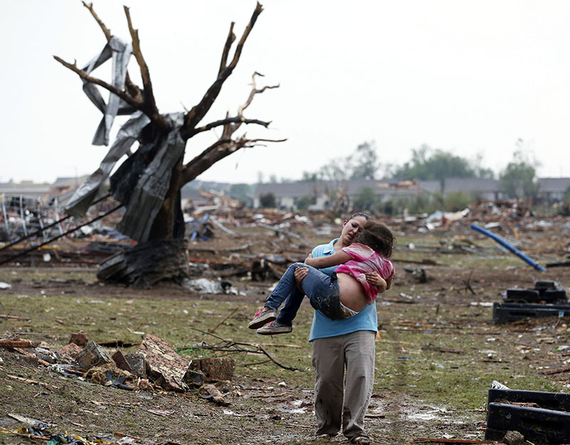 A woman carries a child through a field near the collapsed Plaza Towers Elementary School in Moore, Okla., Monday, May 20, 2013. A tornado as much as a mile wide with winds up to 200 mph roared through the Oklahoma City suburbs Monday, landing a direct...