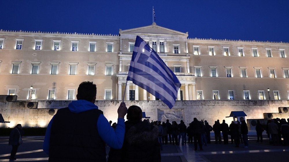 A man holds a Greek flag in front of the Greek parliament in Athens as people gather in support to their government on Feb. 20, 2015.