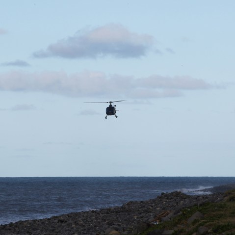 A man watches from the shore as a French Police helicopter flies as part of a search for debris of aircraft in Saint-Andre de la Reunion, in the east of the French Indian Ocean island of La Reunion, on July 30, 2015. (Ouissem Gombra/AFP/Getty)