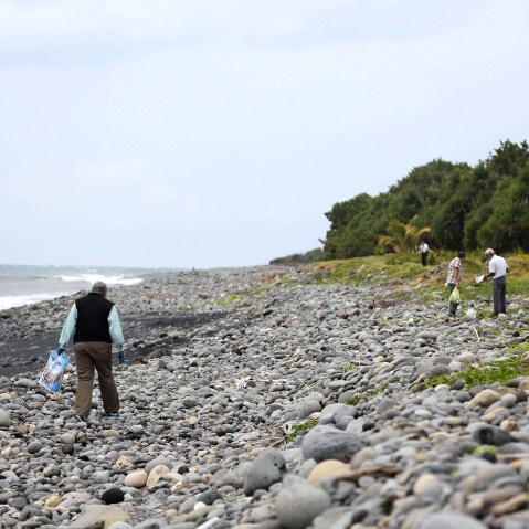 A Malaysian expert (L) looks for debris from the ill-fated Malaysia Airlines flight MH370 on a beach in Saint-Andre de la Reunion, on the French Reunion Island in the Indian Ocean, on Aug. 4, 2015. (Photo by Richard Bouhet/AFP/Getty)