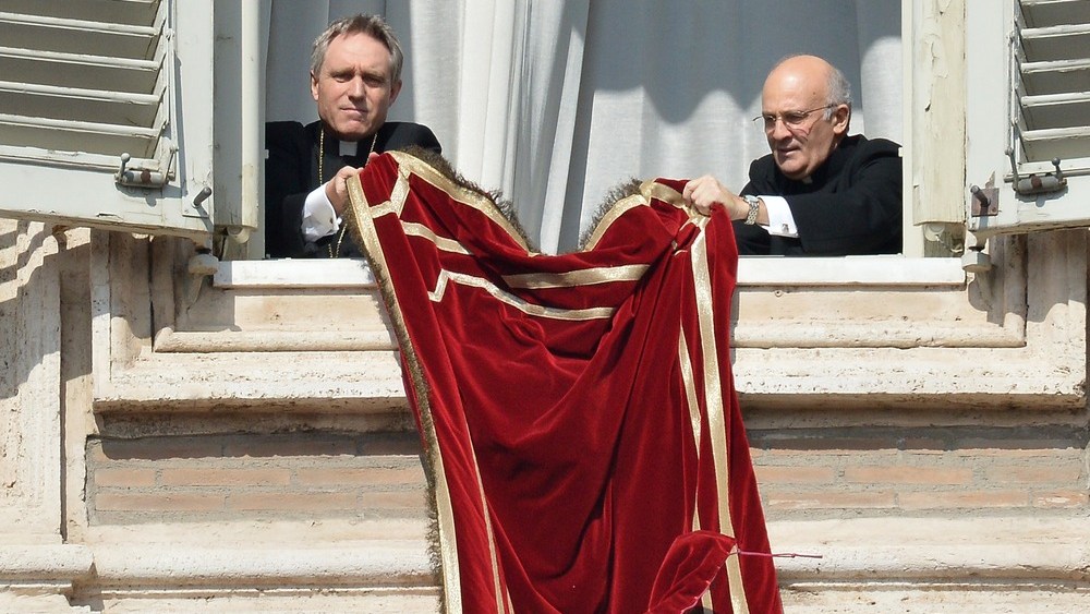 The pope's secretary Georg Gänswein (L) and an unidentified ecclesiastic set the tapestry featuring the tiara on the balcony of St Peter's basilica ahead of Pope Benedict XVI's last Sunday prayers before stepping down on February 24, 2013 at St Peter's...