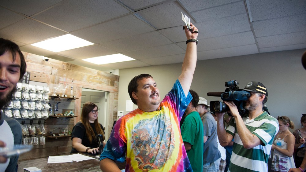 Mike Boyer turns to the crowd outside, showing off the 4 grams of marijuana he bought as the first in line to legally purchase marijuana in Spokane, Wash, July 8, 2014.