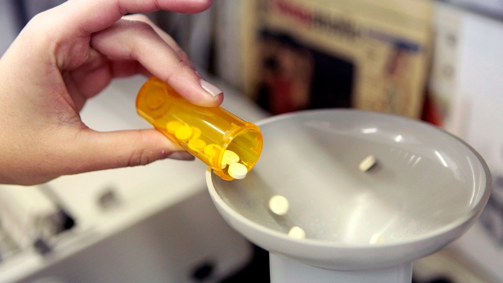 A pharmacy employee dumps pills into a pill counting machine as she fills a prescription while working at a pharmacy in New York