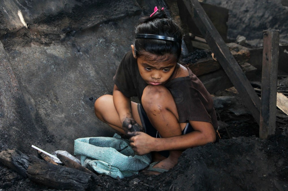 A girl collects pieces of charcoal for sale at a market, in Manila, the Philippines, March 2, 2012. (Photo by Romeo Ranoco/Reuters)