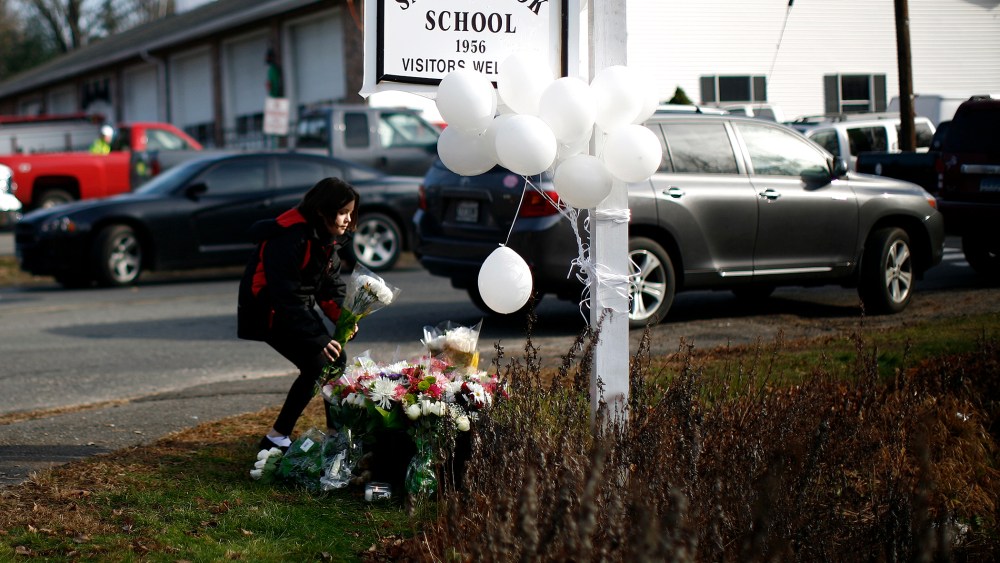 A girl places flowers at a memorial at a sign for Sandy Hook Elementary School in Sandy Hook, Conn.