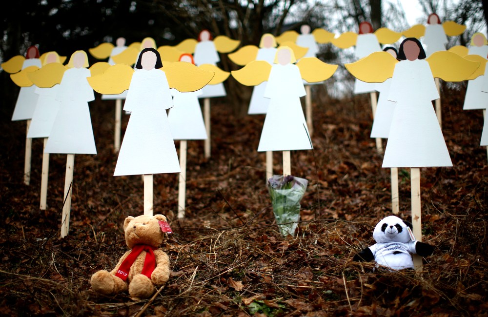 Stuffed animals left by mourners sit beneath some of the 27 wooden angel figures beside a road near the Sandy Hook Elementary School for the victims of a school shooting in Newtown, Connecticut Sunday Dec. 16, 2012.