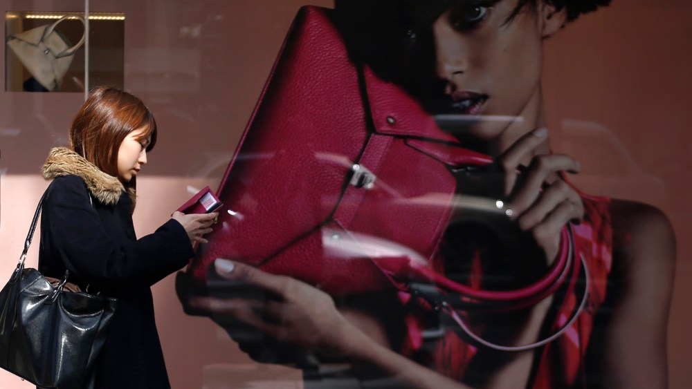 A woman looks at her mobile phone while walking past the display window of a luxury store at Ginza shopping district in Tokyo on Feb. 28, 2014.