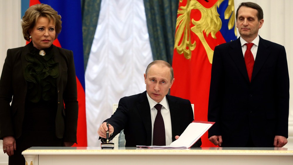 Russian President Vladimir Putin (C) prepares to sign documents as Sergei Naryshkin (R), speaker of the State Duma, Russia's lower parliament house, and Valentina Matviyenko, head of the Federation Council, look on during a ceremony in Moscow's Kremlin Ma