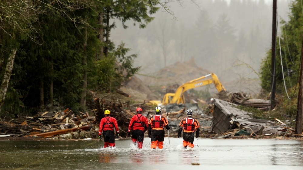 Rescuers walk in floodwaters on Highway 530 as search work continues in the mud and debris from a massive mudslide that struck Oso near Darrington, Washington, March 27, 2014.