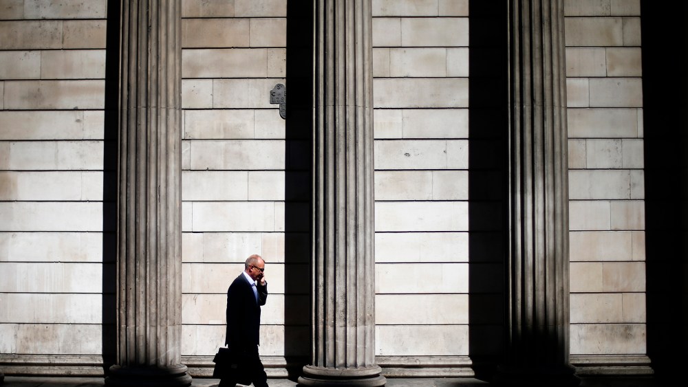 A man speaks on his phone on a sunny morning as he walks past the columns of the Bank of England in the City of London