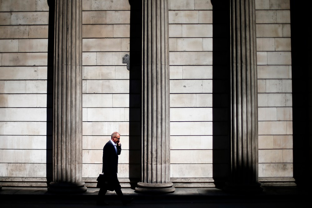 A man speaks on his phone on a sunny morning as he walks past the columns of the Bank of England in the City of London