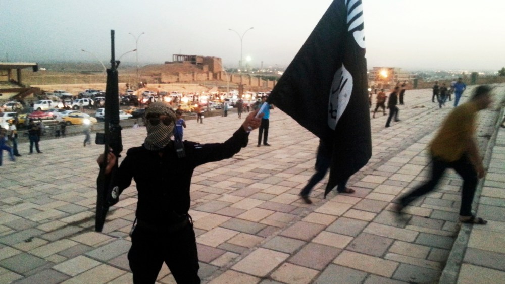 A fighter of the Islamic State of Iraq and the Levant (ISIL) holds an ISIL flag and a weapon on a street in the city of Mosul, June 23, 2014.