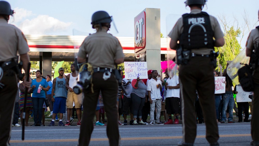Police officers watch as demonstrators protest the death of black teenager Michael Brown in Ferguson, Missouri Aug. 12, 2014.