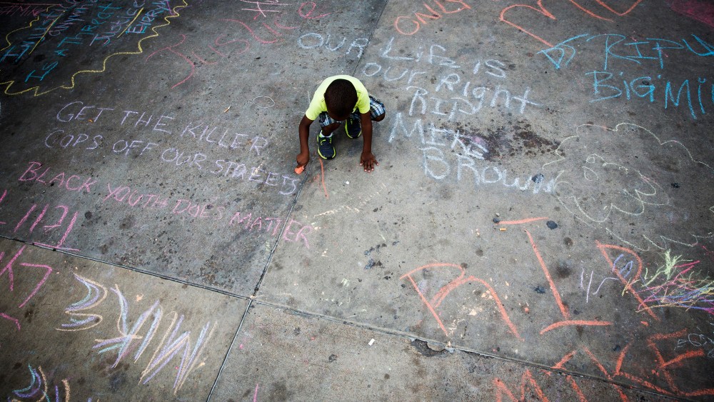 A young boy uses sidewalk chalk to draw on a parking lot filled with memorial slogans during a demonstration to protest the shooting of Michael Brown and the resulting police response to protests, in Ferguson, Mo, Aug. 15, 2014.