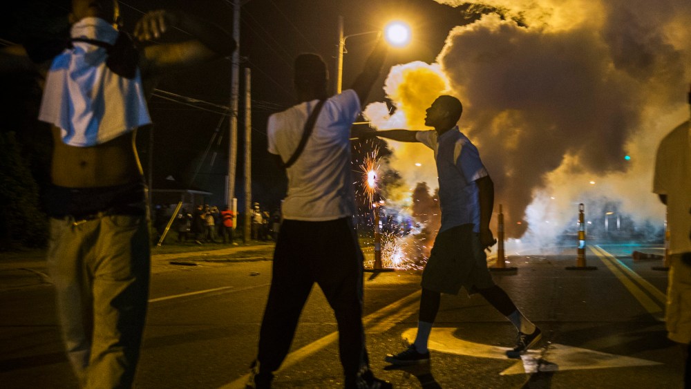 Protesters involved with a more vocal and confrontational group of demonstrators stand and gesture as tear gas is fired, at further protests in reaction to the shooting of Michael Brown near Ferguson, Missouri August 18, 2014.