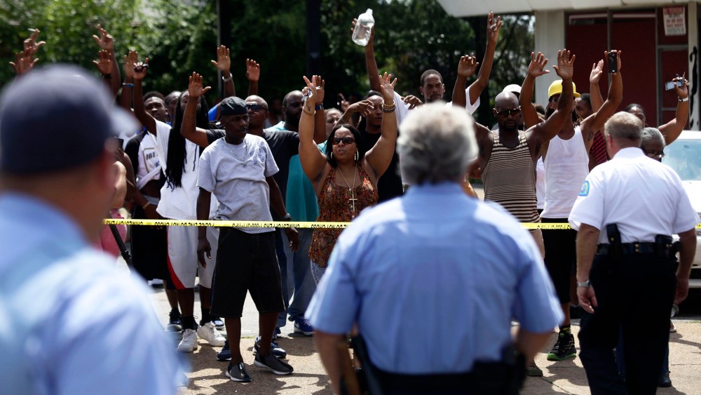 A crowd reacts to St. Louis Police Officers standing outside Golden Shears Barber & Beauty Shop where officers shot a man holding a knife in St. Louis, Mo., Aug. 19, 2014.