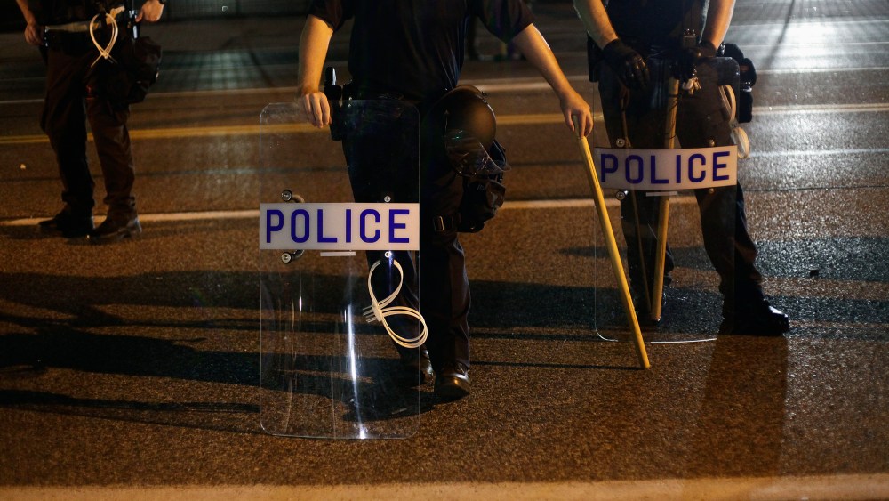 Police officers in riot gear stand in position as demonstrators protest the shooting death of Michael Brown, in Ferguson, Missouri