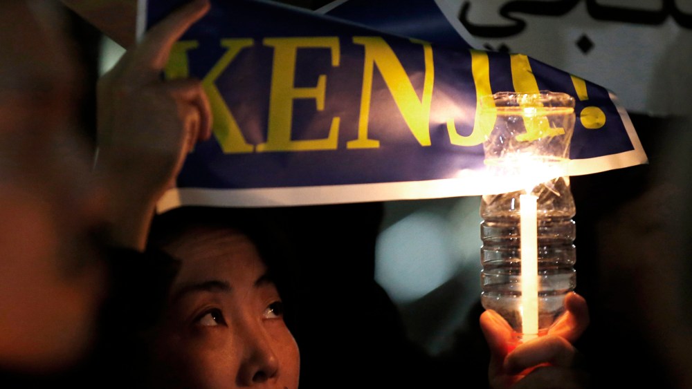 A woman holding a candle and placard takes part in a vigil in front of Prime Minister Shinzo Abe's official residence in Tokyo, Jan. 30, 2015. (Photo by Toru Hanai/Reuters)