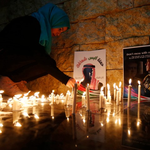A Jordanian woman lights a candle near a poster of Jordan's King Abdullah (R) and a poster depicting Jordanian pilot Muath al-Kasasbeh during a candlelight vigil in Amman on Feb., 7, 2015. (Photo by Muhammad Hamed/Reuters)