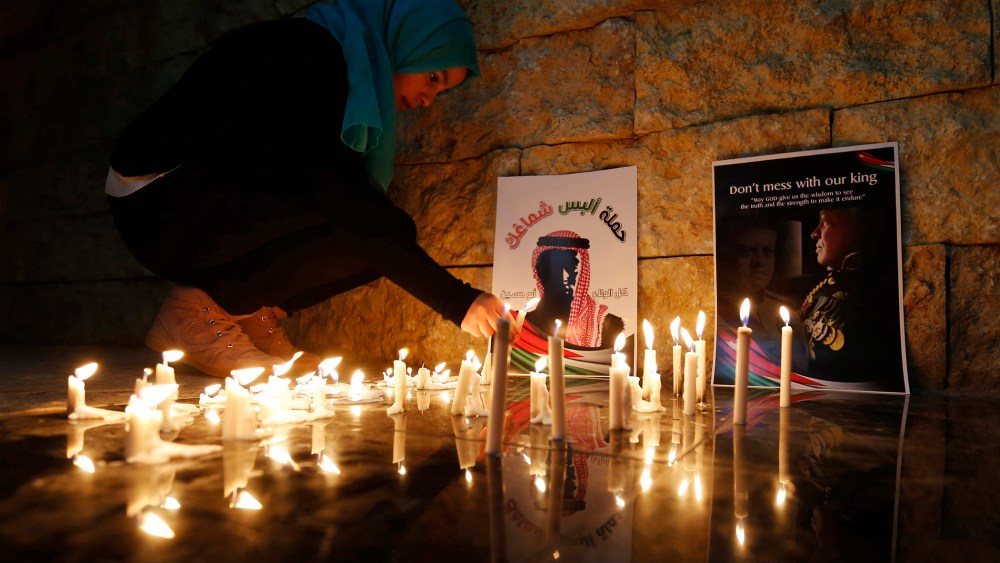 A Jordanian woman lights a candle near a poster of Jordan's King Abdullah (R) and a poster depicting Jordanian pilot Muath al-Kasasbeh during a candlelight vigil in Amman on Feb., 7, 2015. (Photo by Muhammad Hamed/Reuters)