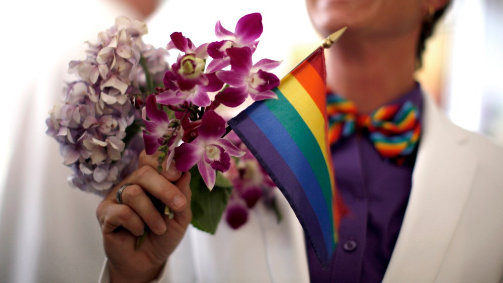 A woman holds a rainbow flag with her bouquet before getting married to her fiancee in West Hollywood, California, July 1, 2013.