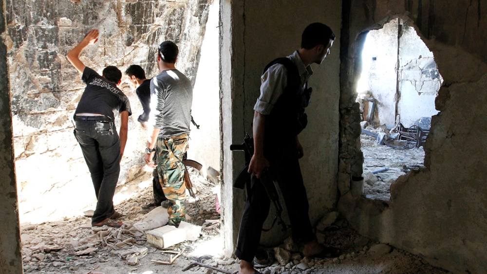 Free Syrian Army fighters peek through holes in a wall at forces loyal to Syria's President Bashar al-Assad as a fellow fighter secures the area in the old city of Aleppo