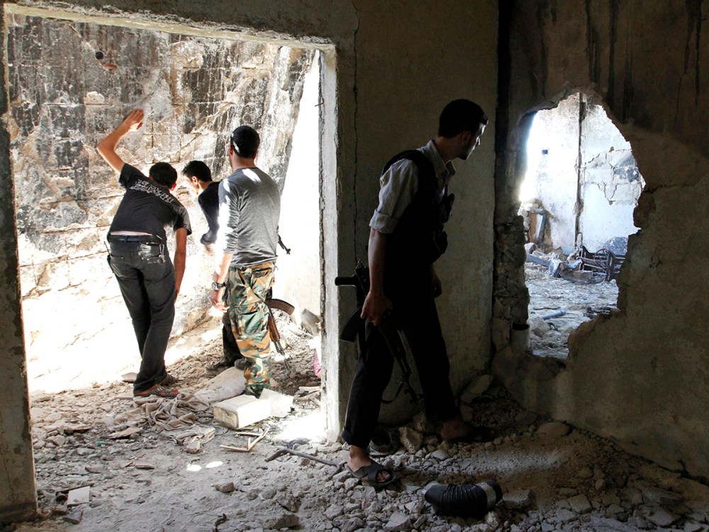 Free Syrian Army fighters peek through holes in a wall at forces loyal to Syria's President Bashar al-Assad as a fellow fighter secures the area in the old city of Aleppo