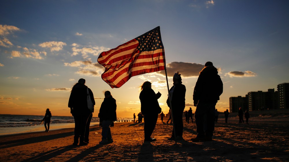 People stand with an American flag during a remembrance ceremony along the beachfront damaged by hurricane Sandy in October 2012 in the borough of Queens in New York
