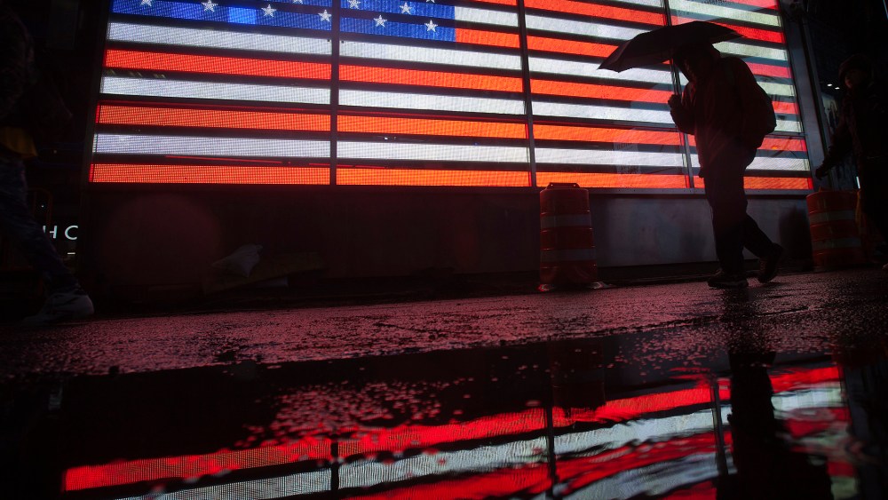 A man walks past a lit US flag with an umbrella at Times Square as it rains in New York, Nov. 26, 2013.
