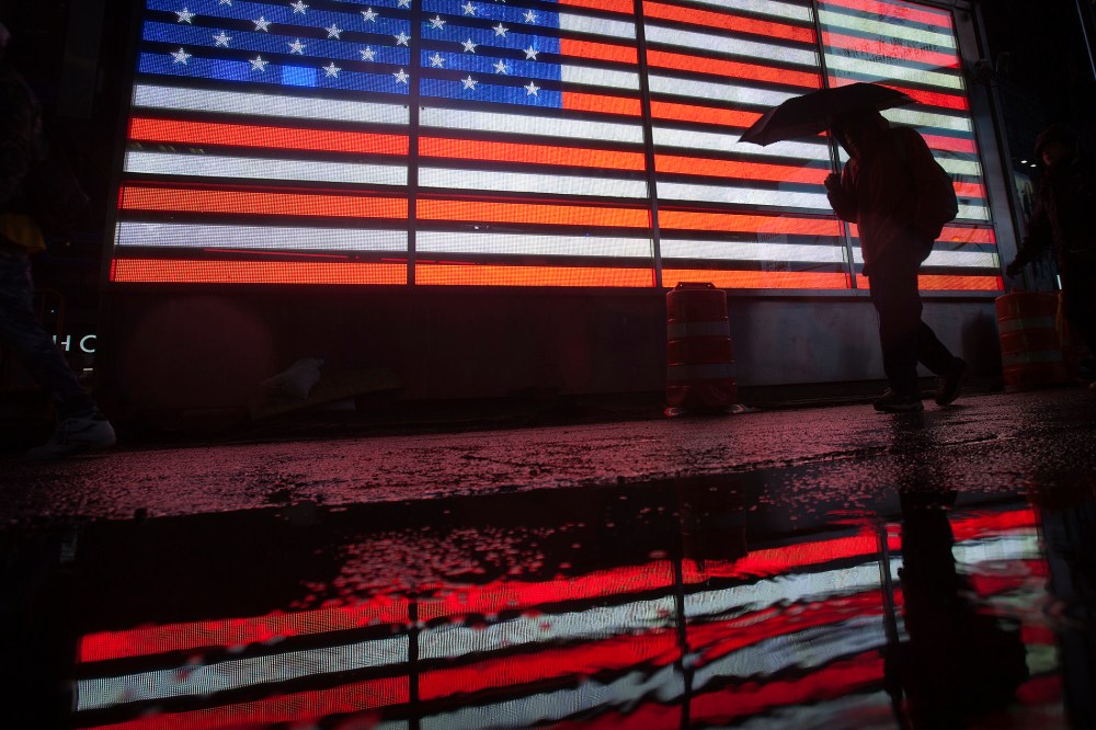 A man walks past a lit US flag with an umbrella at Times Square as it rains in New York, Nov. 26, 2013.