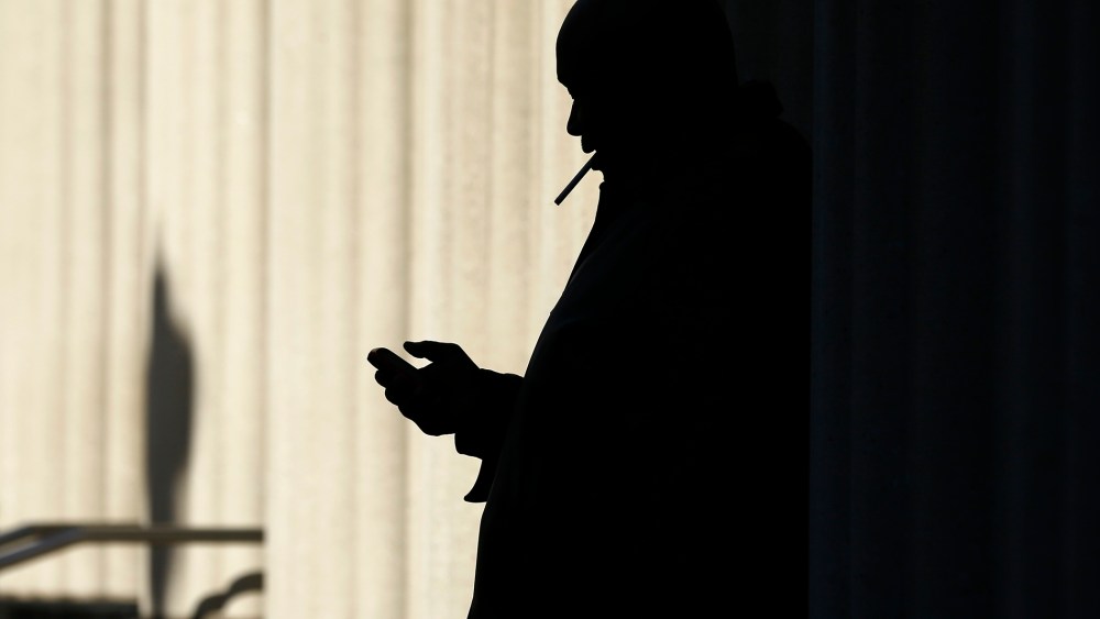 A man on his mobile phone as he smokes a cigarette outside, Dec. 9. 2013, in San Diego, Calif.