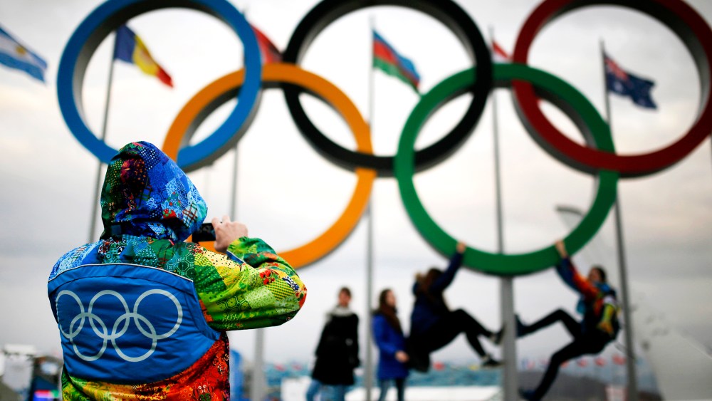 An Olympic volunteer takes pictures of people as they pose under the Olympic rings in Sochi, Jan. 30, 2014.