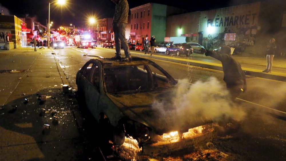 A rioter stands atop a burning car as another man pours fuel onto the fire while Baltimore firefighters behind them fight fires in mutliple burning buildings set ablaze by rioters during clashes in Baltimore, Md., April 27, 2015. (Jim Bourg/Reuters)