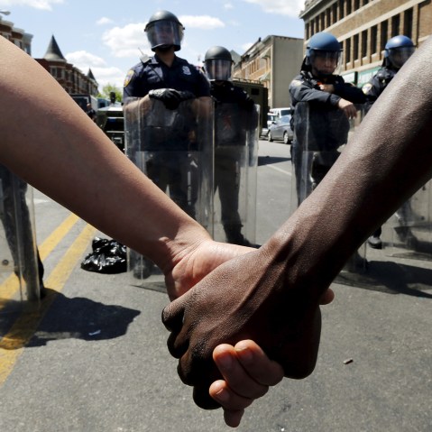 Members of the community hold hands in front of police officers in riot gear outside a recently looted and burned CVS store in Baltimore, Md, on April 28, 2015. (Photo by Jim Bourg/Reuters)