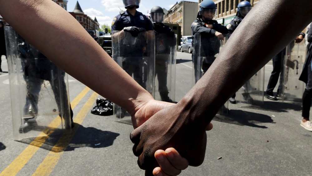 Members of the community hold hands in front of police officers in riot gear outside a recently looted and burned CVS store in Baltimore, Md, on April 28, 2015. (Photo by Jim Bourg/Reuters)