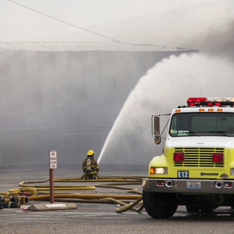 Firefighters rest as their colleague continues to battle flames that burned through the night at a commercial building that was ignited by the Sleepy Hollow fire in Wenatchee, Washington June 29, 2015. (Photo by David Ryder/Reuters)