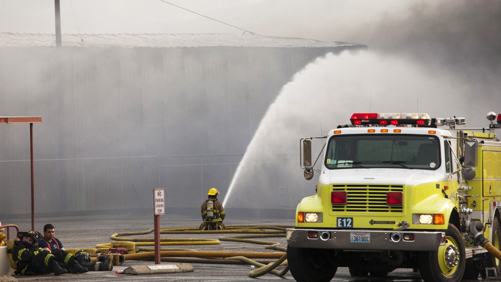 Firefighters rest as their colleague continues to battle flames that burned through the night at a commercial building that was ignited by the Sleepy Hollow fire in Wenatchee, Washington June 29, 2015. (Photo by David Ryder/Reuters)