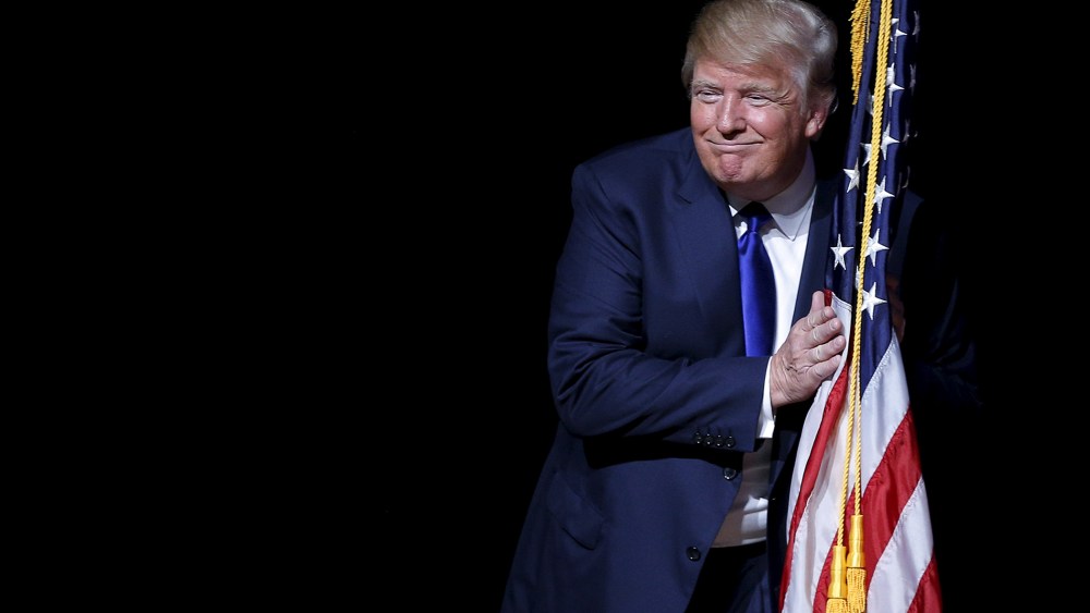 U.S. Republican presidential candidate Donald Trump hugs a U.S. flag as he takes the stage for a campaign town hall meeting in Derry, N.H., Aug. 19, 2015. (Photo by Brian Snyder/Reuters)