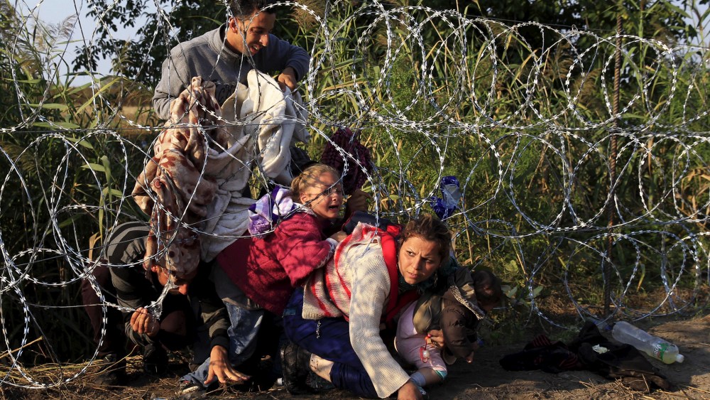 Syrian migrants cross under a fence as they enter Hungary at the border with Serbia, near Roszke, Aug. 27, 2015. (Photo by Bernadett Szabo/Reuters)