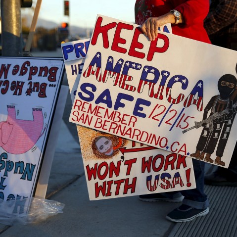 Signs protesting ISIS and President Obama are held across from a makeshift memorial for victims of the San Bernardino shooting in San Bernardino, Calif., on Dec. 18, 2015. (Photo by Patrick Fallon/Reuters)