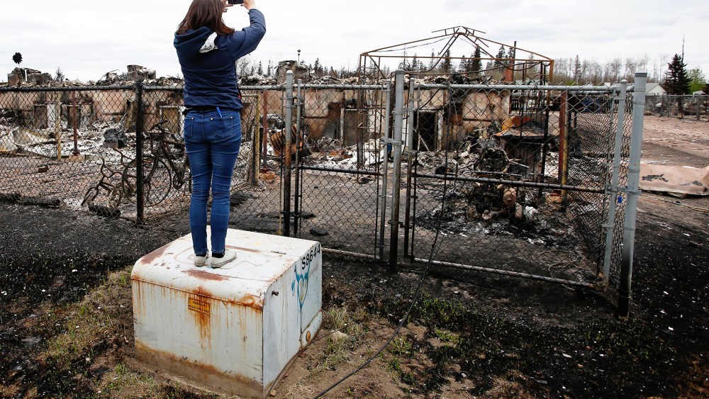 A woman takes photos of the burned remains of a house in the Abasand neighbourhood of Fort McMurray, Alberta, Canada, May 9, 2016 after wildfires forced the evacuation of the town. (Photo by Chris Wattie/Reuters)