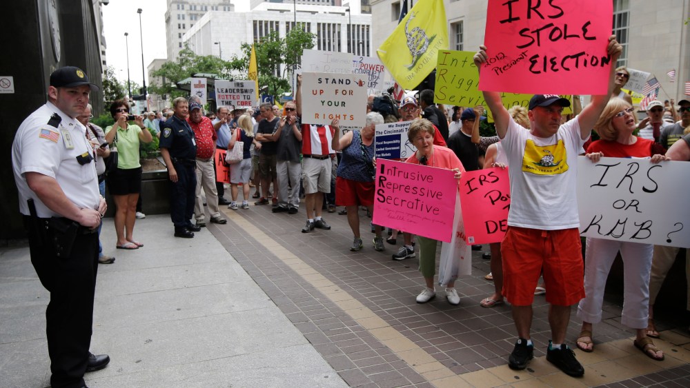 A federal officer watches as tea party activists demonstrate outside the John Weld Peck Federal Building, Tuesday, May 21, 2013, in Cincinnati. The building houses the main offices for the Internal Revenue Service in the city and is tied to the...