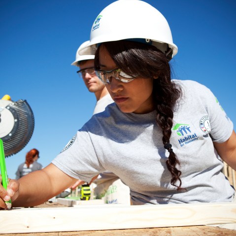 AmeriCorps volunteer Victoria Piar from Habitat for Humanity of Orange County, saws lumber for a new house frame.