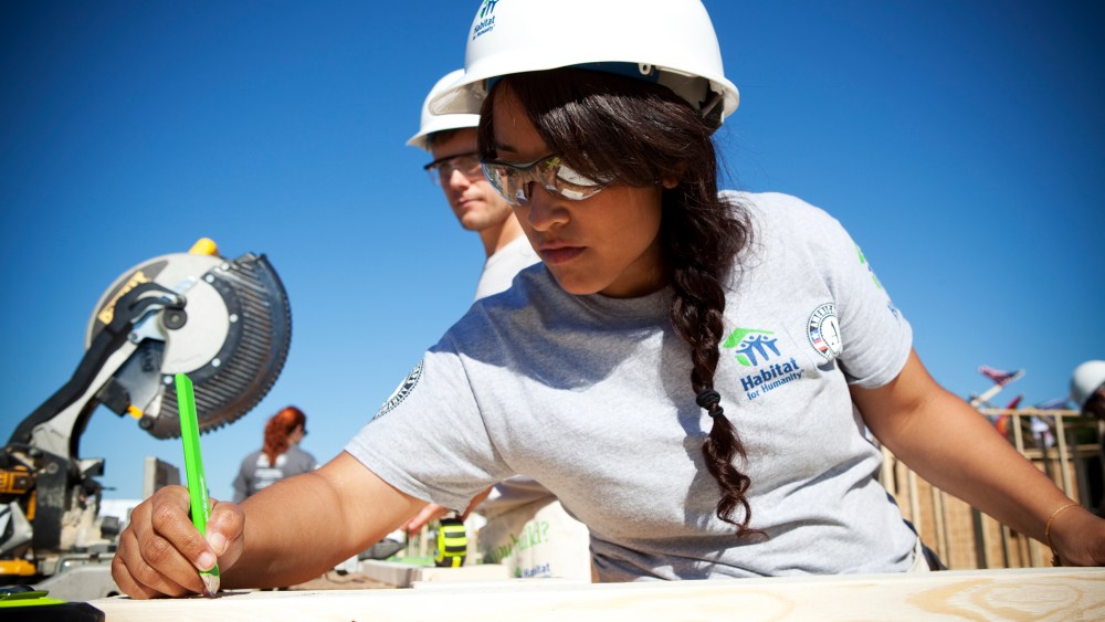 AmeriCorps volunteer Victoria Piar from Habitat for Humanity of Orange County, saws lumber for a new house frame.