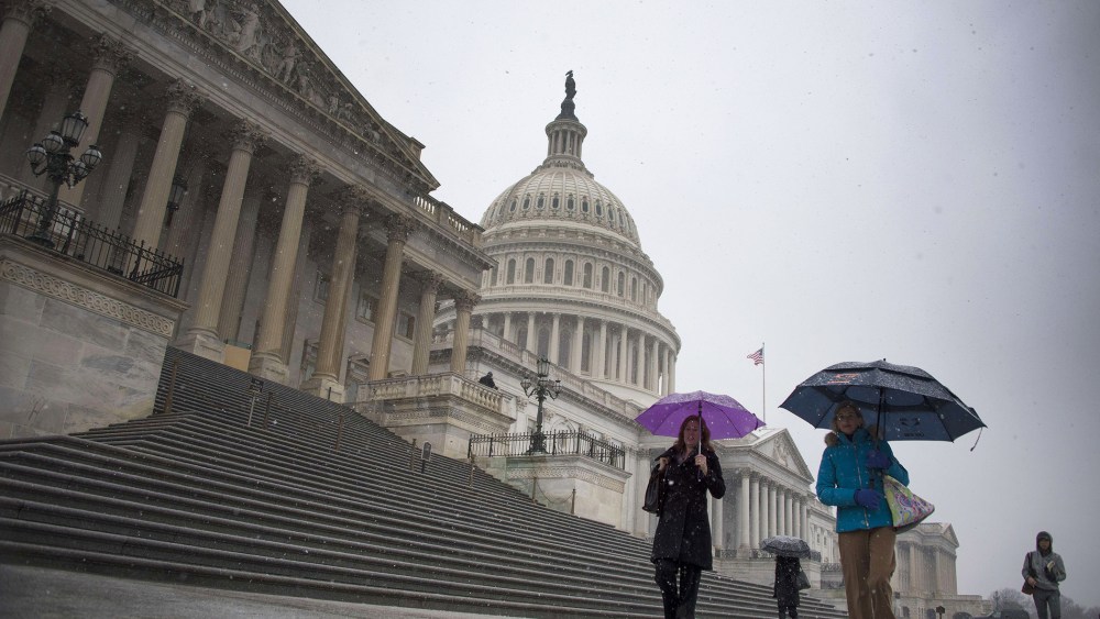 People hold umbrellas as they walk past the US Capitol Building in Washington, DC, Dec. 10, 2013.